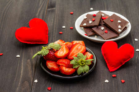 Valentine's Day romantic concept. Chocolate, fresh ripe strawberry, red felt hearts. Sweet dessert for lovers. Black wooden backgroundの写真素材