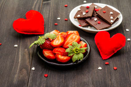Valentine's Day romantic concept. Chocolate, fresh ripe strawberry, red felt hearts. Sweet dessert for lovers. Black wooden background, close upの写真素材
