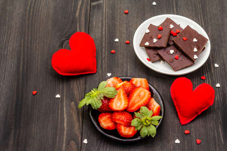 Valentine's Day romantic concept. Chocolate, fresh ripe strawberry, red felt hearts. Sweet dessert for lovers. Black wooden backgroundの写真素材