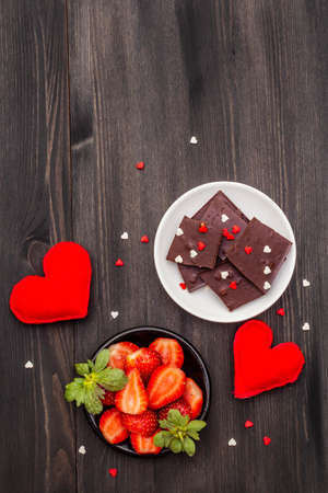 Valentine's Day romantic concept. Chocolate, fresh ripe strawberry, red felt hearts. Sweet dessert for lovers. Black wooden background, top view, copy spaceの写真素材