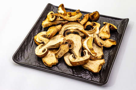 Dried porcini mushrooms isolated on white background. Traditional ingredient for cooking healthy food. Black ceramic plate, close upの写真素材