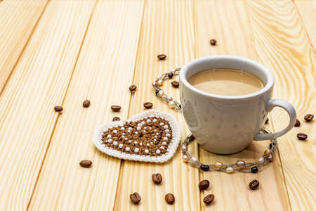 Valentine's Day concept. Cup of coffee, knitted heart, string of pearl beads. Romantic breakfast and gift on wooden boards background, copy spaceの写真素材