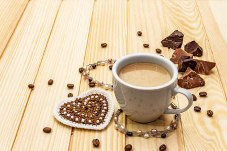 Valentine's Day concept. Cup of coffee, chocolate, knitted heart, string of pearl beads. Romantic breakfast and gift on wooden boards background, copy spaceの写真素材