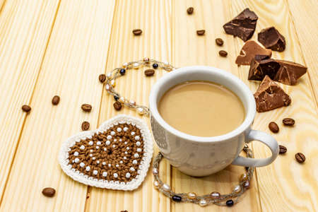 Valentine's Day concept. Cup of coffee, chocolate, knitted heart, string of pearl beads. Romantic breakfast and gift on wooden boards background, copy space, top viewの写真素材