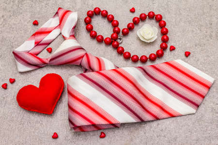 Valentines Day concept. Red felt hearts, women beads, men tie. Stone concrete background, top view,...