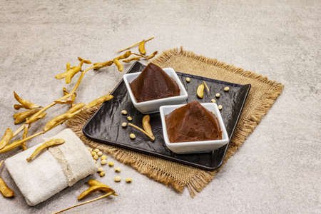 Miso paste, traditional Japanese seasoning. Two types, dark and light brown with dry soya beans. Sackcloth, bag, pods. Stone concrete background, copy spaceの写真素材