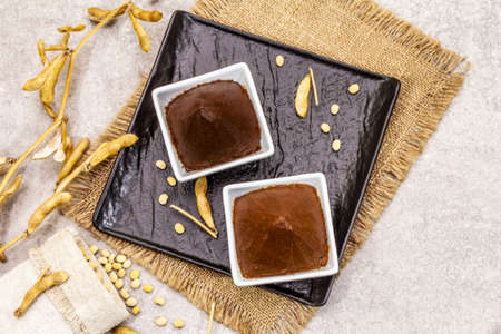 Miso paste, traditional Japanese seasoning. Two types, dark and light brown with dry soya beans. Sackcloth, bag, pods. Stone concrete background, top view, copy spaceの写真素材