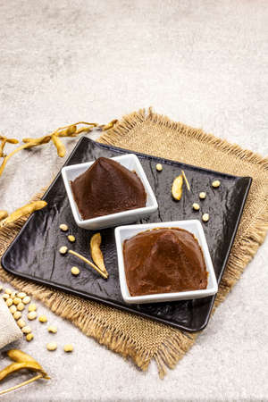 Miso paste, traditional Japanese seasoning. Two types, dark and light brown with dry soya beans. Sackcloth, bag, pods. Stone concrete background, copy spaceの写真素材
