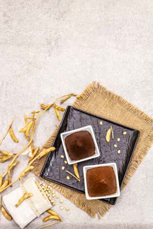 Miso paste, traditional Japanese seasoning. Two types, dark and light brown with dry soya beans. Sackcloth, bag, pods. Stone concrete background, top view, copy spaceの写真素材
