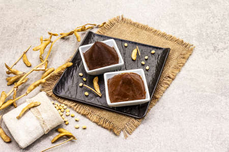 Miso paste, traditional Japanese seasoning. Two types, dark and light brown with dry soya beans. Sackcloth, bag, pods. Stone concrete background, copy spaceの写真素材