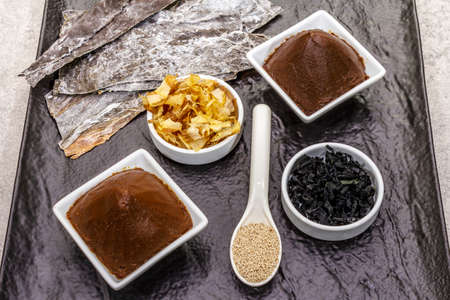 Set of traditional Japanese ingredient for cooking basic dashi broth. Algae kombu and wakame, miso paste, katsuobushi and dry granules. Black ceramic plate background, top viewの写真素材