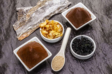 Set of traditional Japanese ingredient for cooking basic dashi broth. Algae kombu and wakame, miso paste, katsuobushi and dry granules. Black ceramic plate background, top viewの写真素材
