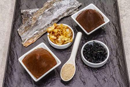Set of traditional Japanese ingredient for cooking basic dashi broth. Algae kombu and wakame, miso paste, katsuobushi and dry granules. Black ceramic plate background, top viewの写真素材