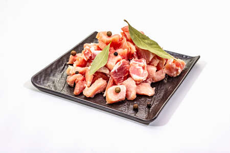 Diced raw pork meat, isolated on white background. Fresh pieces, spices on black ceramic plate, copy space, close upの写真素材
