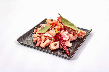 Diced raw pork meat, isolated on white background. Fresh pieces, spices on black ceramic plate, copy spaceの写真素材