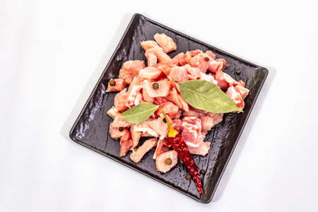 Diced raw pork meat, isolated on white background. Fresh pieces, spices on black ceramic plate, copy space, top viewの写真素材