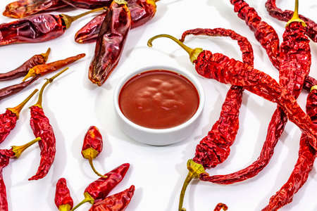 Spicy chili sauce in bowl isolated on white background. Different varieties of dry hot peppers, main ingredient for preparation. Cooking backdrop, mockup, close upの写真素材