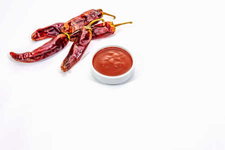 Spicy chili sauce in bowl isolated on white background. Different varieties of dry hot peppers, main ingredient for preparation. Cooking backdrop, mockup, copy spaceの写真素材