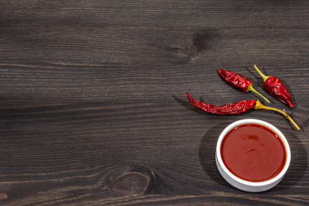 Hot chili sauce in bowl with dry hot peppers, main ingredient for preparation. Black wooden cooking background, copy spaceの写真素材