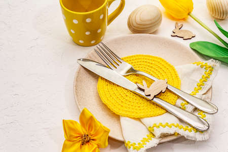 Easter table setting on textured white putty background. Spring holiday card template. Cutlery,...