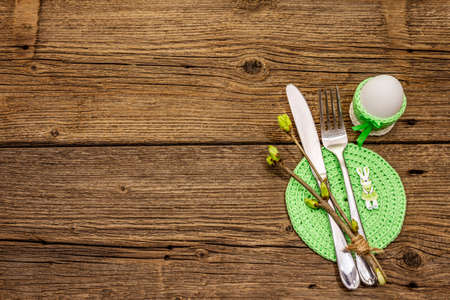 Easter table setting on antique wooden background. Spring holiday card template. Cutlery, crochet napkin, egg, twigs of lilac, copy space, top viewの写真素材