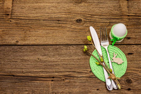 Easter table setting on antique wooden background. Spring holiday card template. Cutlery, crochet napkin, egg, twigs of lilac, copy space, top viewの写真素材