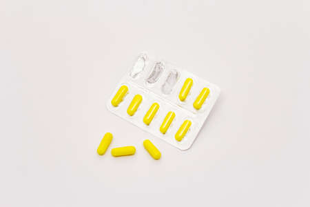 Pharmaceutical tablets, yellow capsules in blister pack isolated on white background. Treatment of various diseases, traditional medicineの写真素材