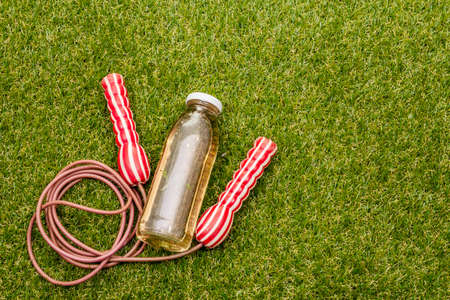 Jump rope and bottle of refreshment detox water. Sport equipment on green grass. Physical activity...