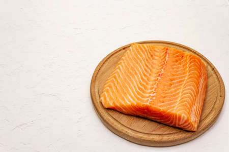Fresh salmon filet. Wooden cutting board, concept of a healthy and balanced diet. White putty background, copy spaceの写真素材