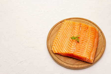 Fresh salmon filet. Wooden cutting board, concept of a healthy and balanced diet. White putty background, copy spaceの写真素材