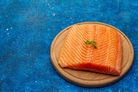 Fresh salmon filet. Wooden cutting board, concept of a healthy and balanced diet. Blue marine background, copy spaceの写真素材