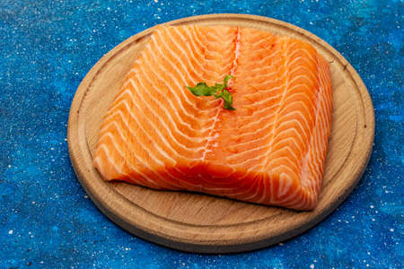 Fresh salmon filet. Wooden cutting board, concept of a healthy and balanced diet. Blue marine background, close upの写真素材