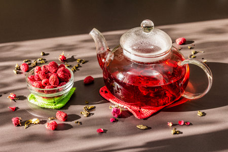 Sunny morning breakfast. Sweet raspberry green tea in glass kettle with dry fruits, flowers and leaves. Trendy black stone backgroundの写真素材