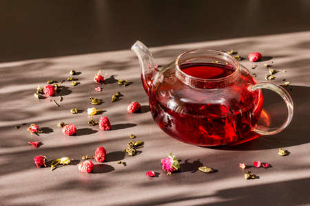 Sunny morning breakfast. Sweet raspberry green tea in glass kettle with dry fruits, flowers and...