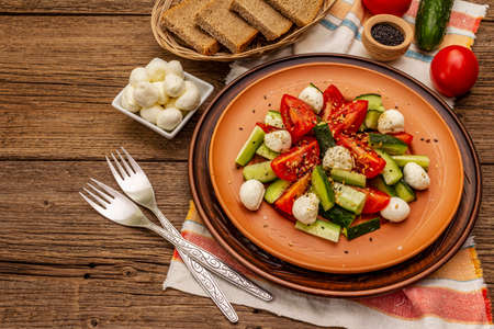Fresh salad from tomato, cucumber and baby mozzarella. Sunny lunch with crusty bread. Old wooden boards backgroundの写真素材