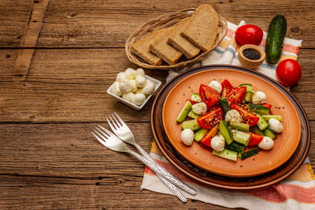 Fresh salad from tomato, cucumber and baby mozzarella. Sunny lunch with crusty bread. Old wooden boards backgroundの写真素材
