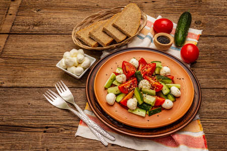 Fresh salad from tomato, cucumber and baby mozzarella. Sunny lunch with crusty bread. Old wooden boards backgroundの写真素材