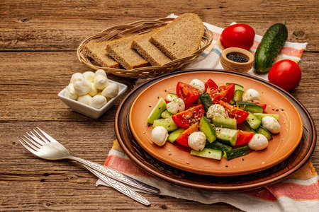 Fresh salad from tomato, cucumber and baby mozzarella. Sunny lunch with crusty bread. Old wooden boards backgroundの写真素材