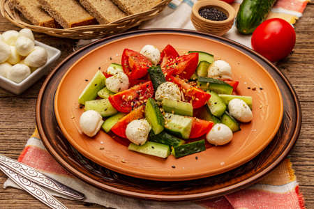 Fresh salad from tomato, cucumber and baby mozzarella. Sunny lunch with crusty bread. Old wooden boards backgroundの写真素材