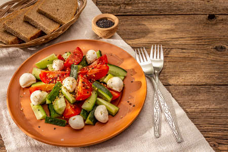 Fresh salad from tomato, cucumber and baby mozzarella. Sunny lunch with crusty bread. Old wooden boards backgroundの写真素材