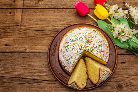 Easter cake on old wooden table. Traditional Orthodox festive bread, cut pieces, artificial decor