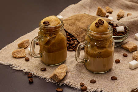 Dalgona coffee in mason jar. Korean fluffy whipped coffee beverage. Trendy quarantine drink, sugar and coffee beans on black stone concrete backgroundの写真素材