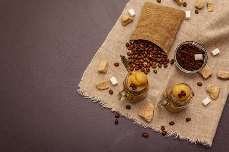Dalgona coffee in mason jar. Korean fluffy whipped coffee beverage. Trendy quarantine drink, sugar and coffee beans on black stone concrete background, top viewの写真素材