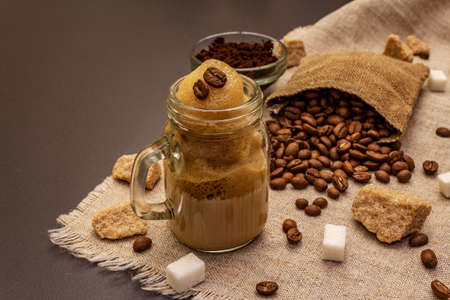 Dalgona coffee in mason jar. Korean fluffy whipped coffee beverage. Trendy quarantine drink, sugar and coffee beans on black stone concrete backgroundの写真素材