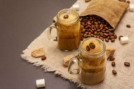 Dalgona coffee in mason jar. Korean fluffy whipped coffee beverage. Trendy quarantine drink, sugar and coffee beans on black stone concrete backgroundの写真素材