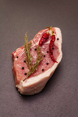 Raw pork steak on trendy black stone concrete background. Spices, sea salt, rosemary, chili pepper, close upの写真素材