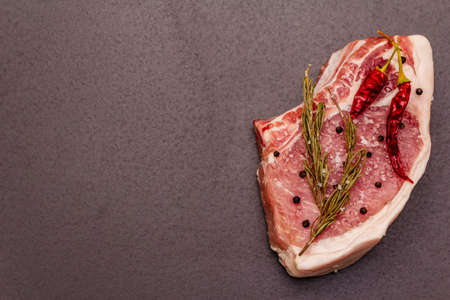 Raw pork steak on trendy black stone concrete background. Spices, sea salt, rosemary, chili pepper, top view, copy spaceの写真素材