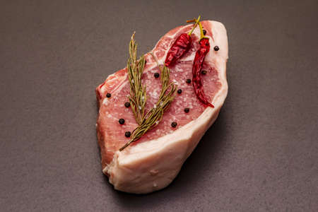 Raw pork steak on trendy black stone concrete background. Spices, sea salt, rosemary, chili pepper, close upの写真素材