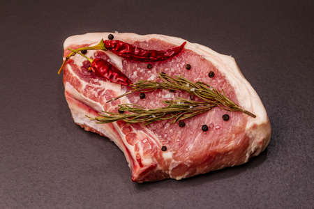 Raw pork steak on trendy black stone concrete background. Spices, sea salt, rosemary, chili pepper, close upの写真素材