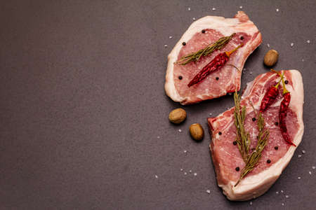 Raw pork steaks on trendy black stone concrete background. Spices, sea salt, rosemary, chili pepper, top view, copy spaceの写真素材